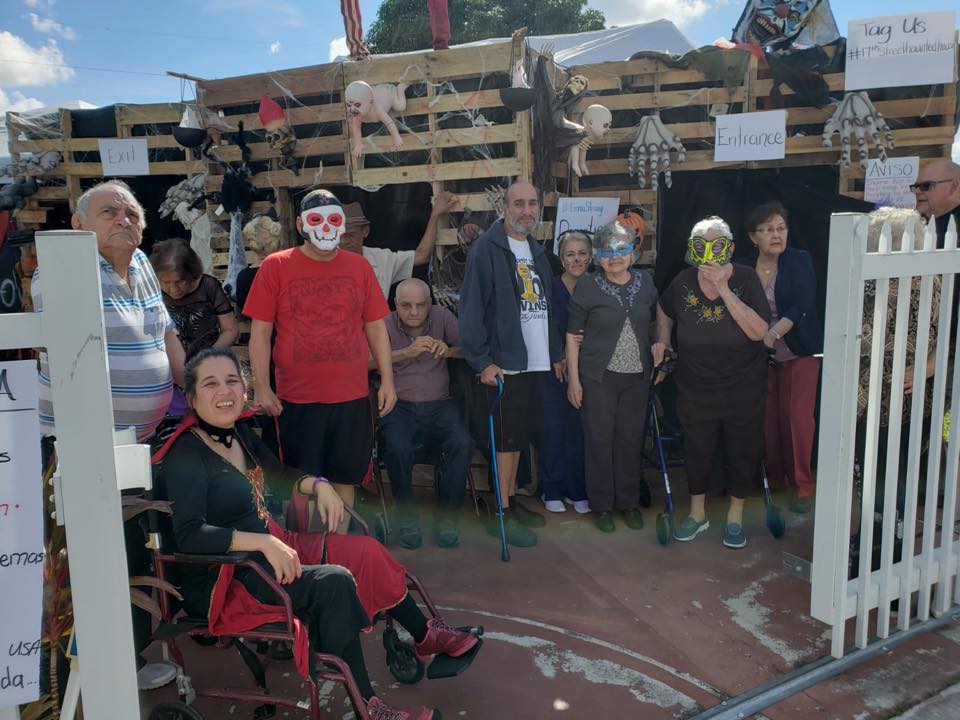 Group of people with some in costume, posing in front of a pallet structure.
