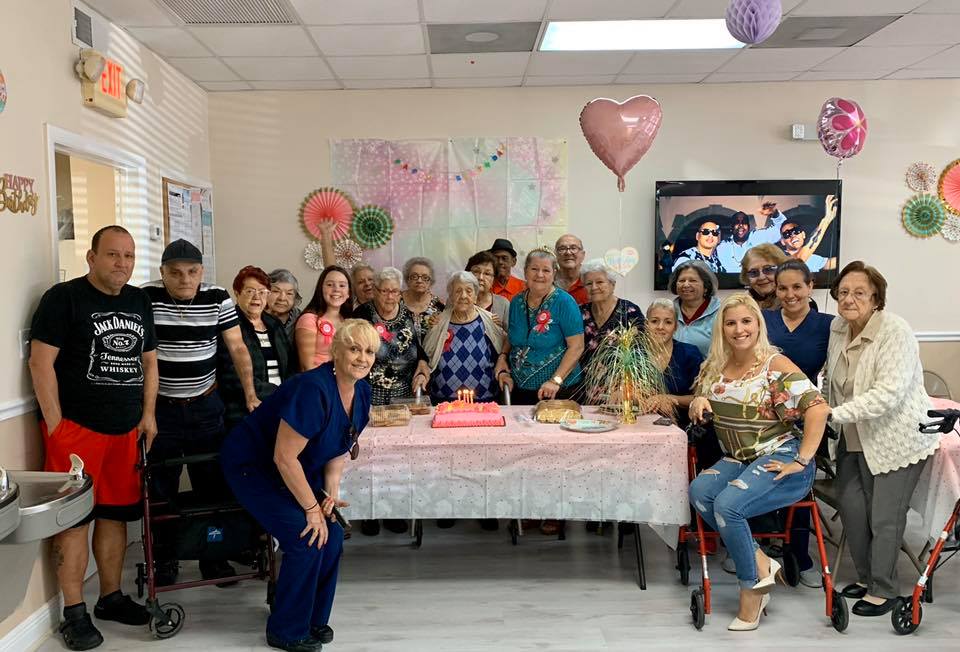 A group celebrates a birthday at a facility, with a cake on a decorated table.