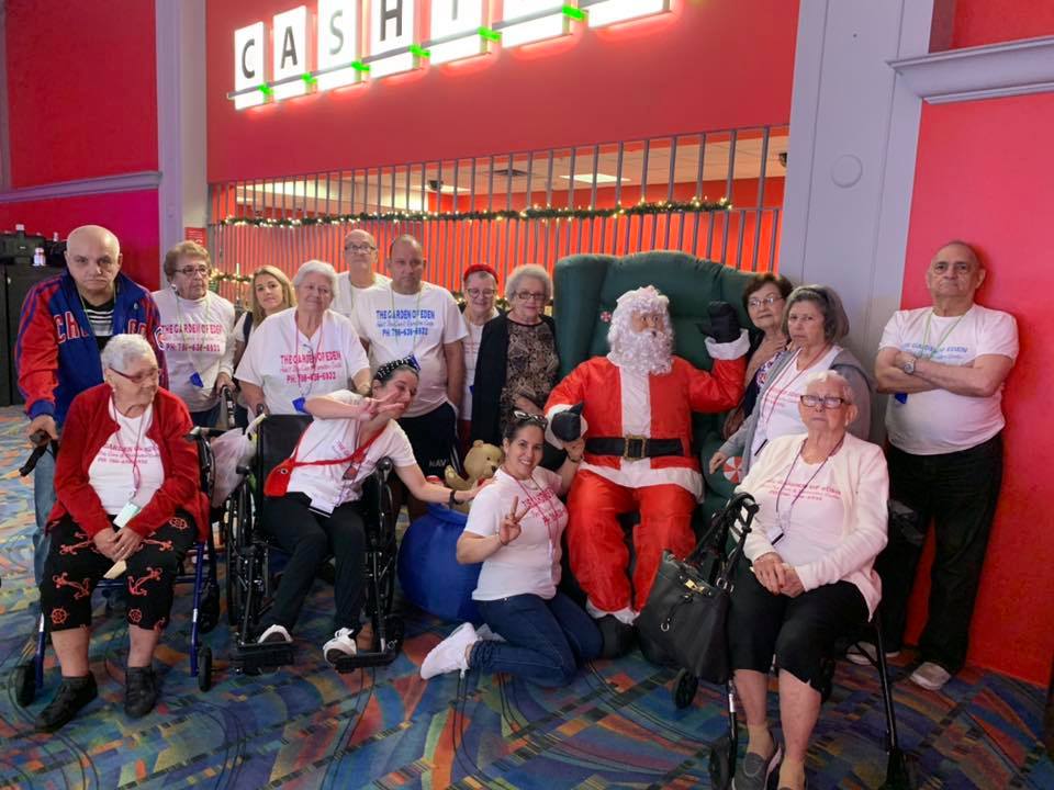 A group poses with Santa inside a building. Some are in wheelchairs, wearing white shirts, and smiling.