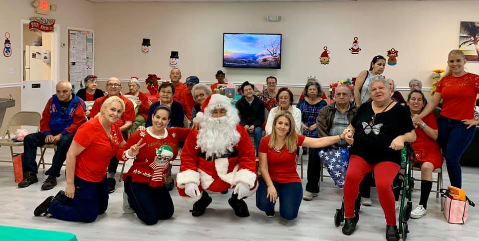 Group photo with Santa, residents and staff, wearing red, in a decorated room.