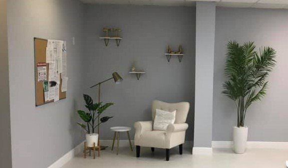 Gray office corner with an armchair, plants, shelves, and a bulletin board.