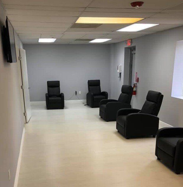 Waiting room with gray walls, light-colored floor, black recliners, and a door.