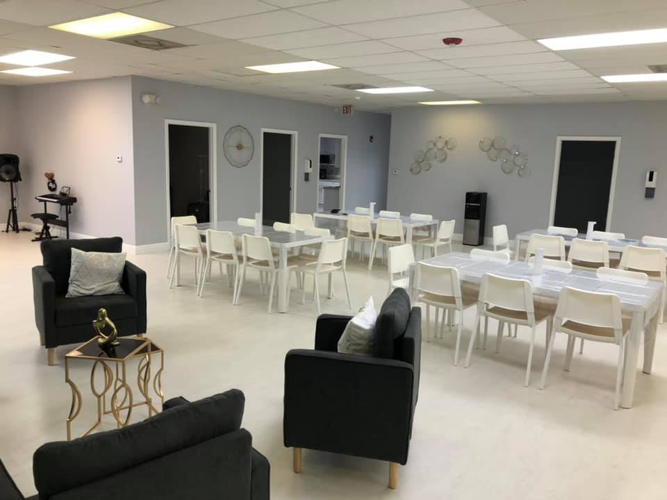 Spacious room with seating areas and multiple tables set for an event; gray walls, white chairs.