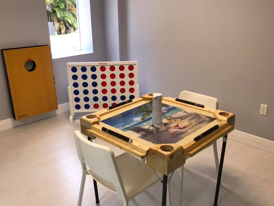 Game room with domino table, Connect Four, cornhole board, and two white chairs.