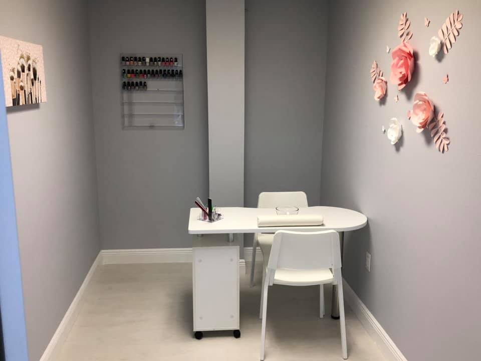 Small nail salon with a white table and chairs against gray walls. Nail polish rack on the wall.