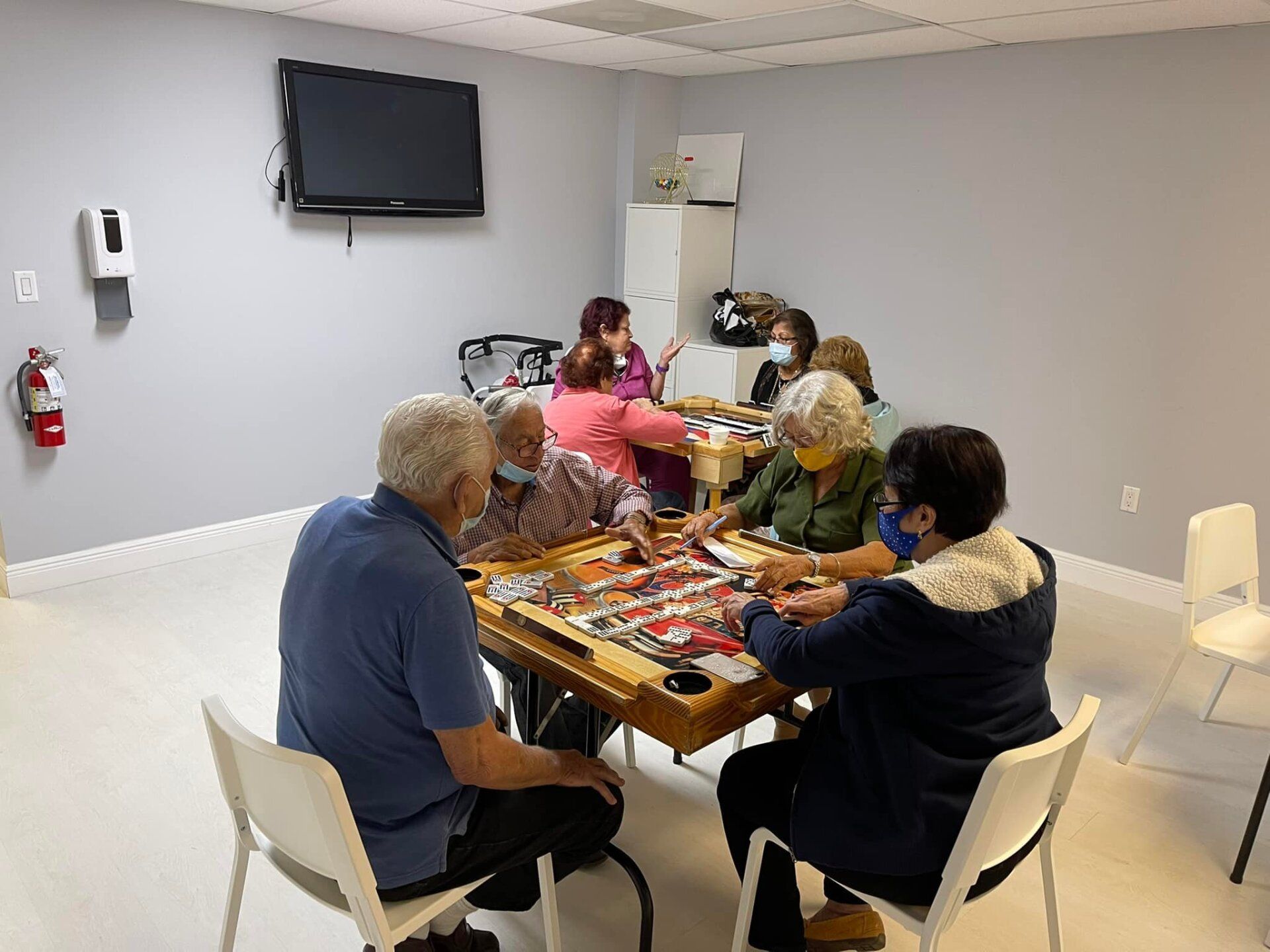 Group of people playing a game around a table in a room. A TV is on the wall.