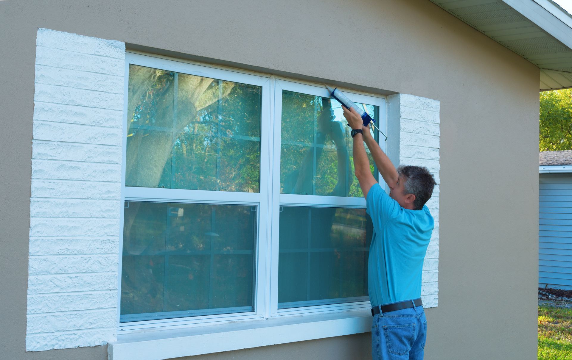 Person cleaning a white-framed window on a house exterior with a squeegee