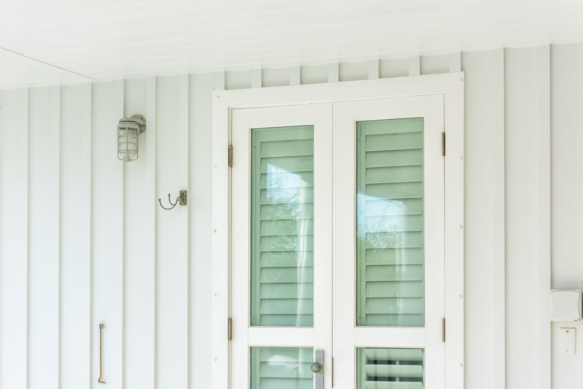 White porch wall with a glass-paneled front door and a small lantern light
