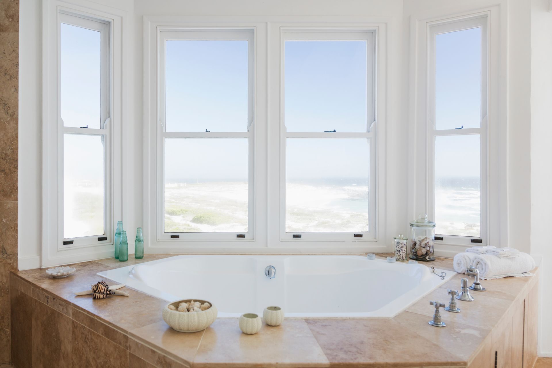 Luxury bathroom with large windows, a corner soaking tub, and a view of the ocean