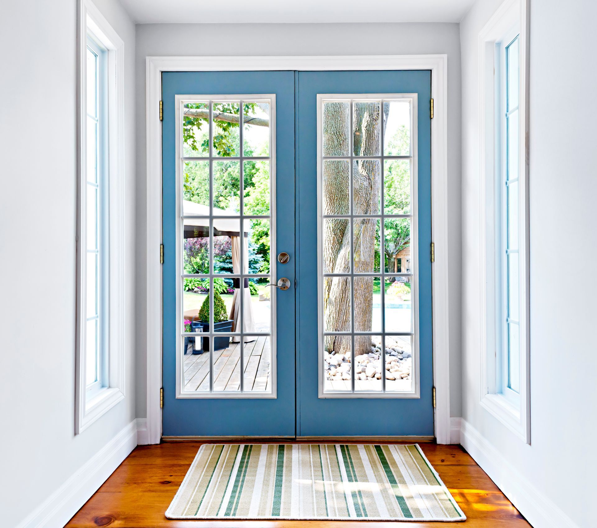 Bright hallway with blue French doors, white walls, hardwood floor, and a striped rug.