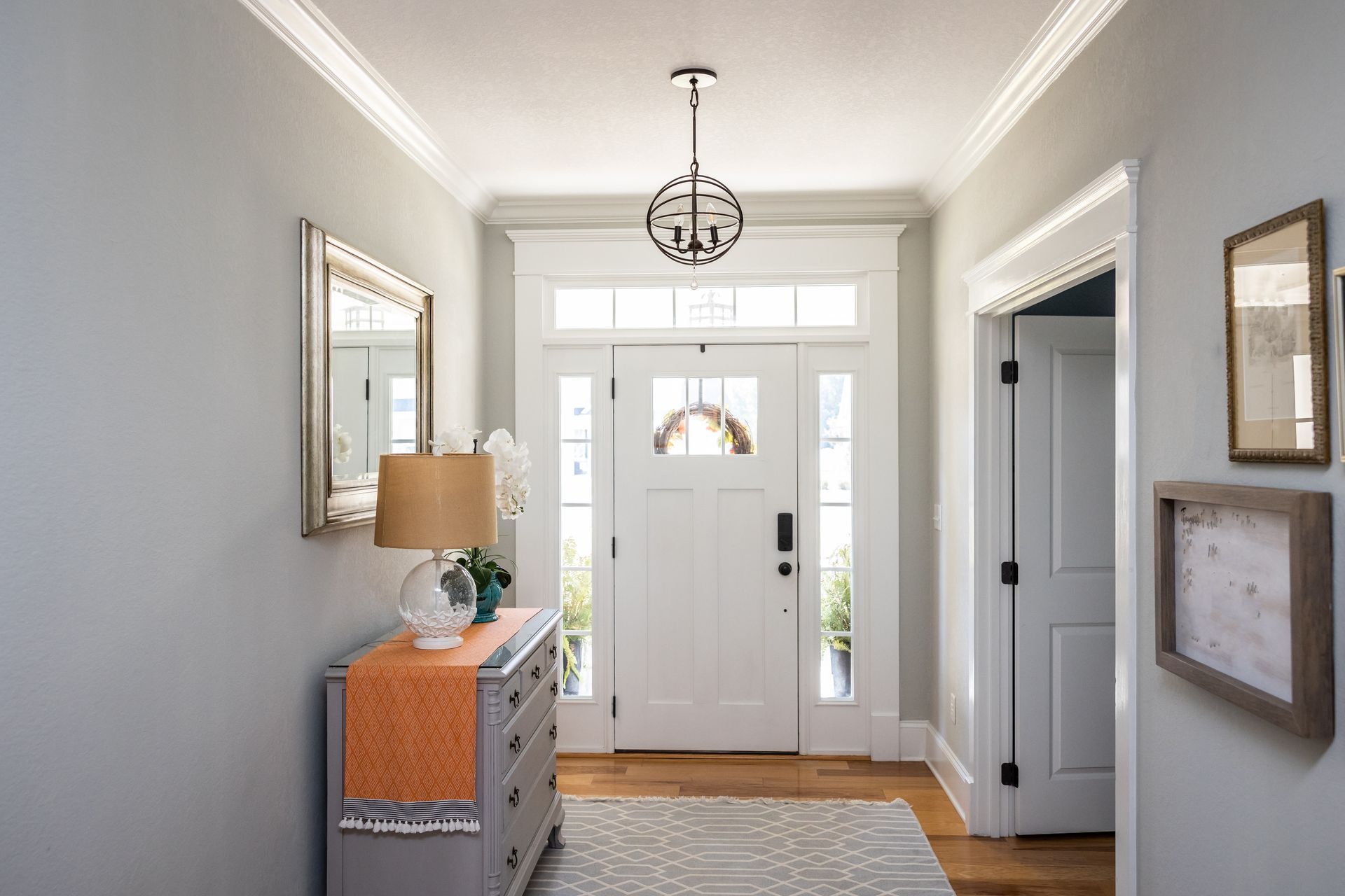 Bright entryway with white front door, gray walls, patterned rug, and a blue dresser with lamp and mirror.