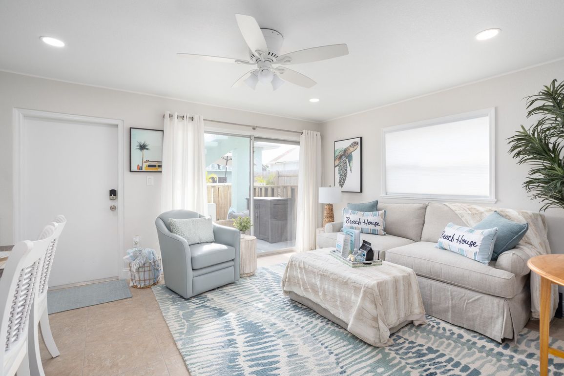 Bright living room with beige sectional, blue accents, armchair, and sliding glass door to balcony.