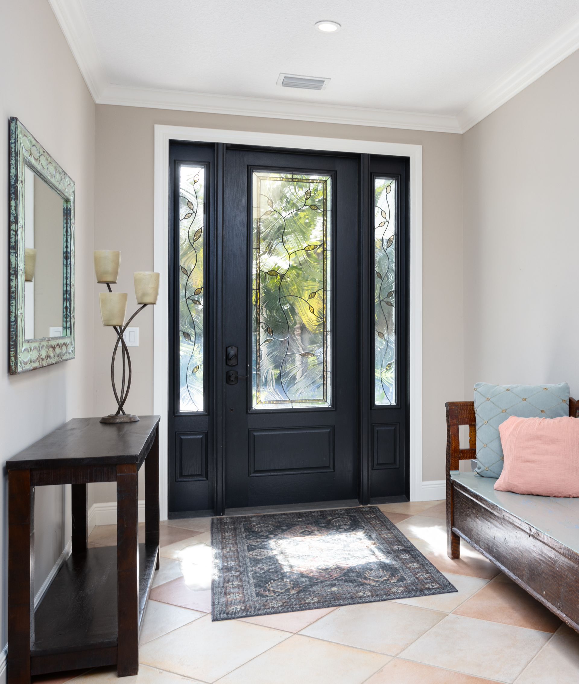 Bright entryway with black double front doors, a console table, mirror, and a bench with pillows.