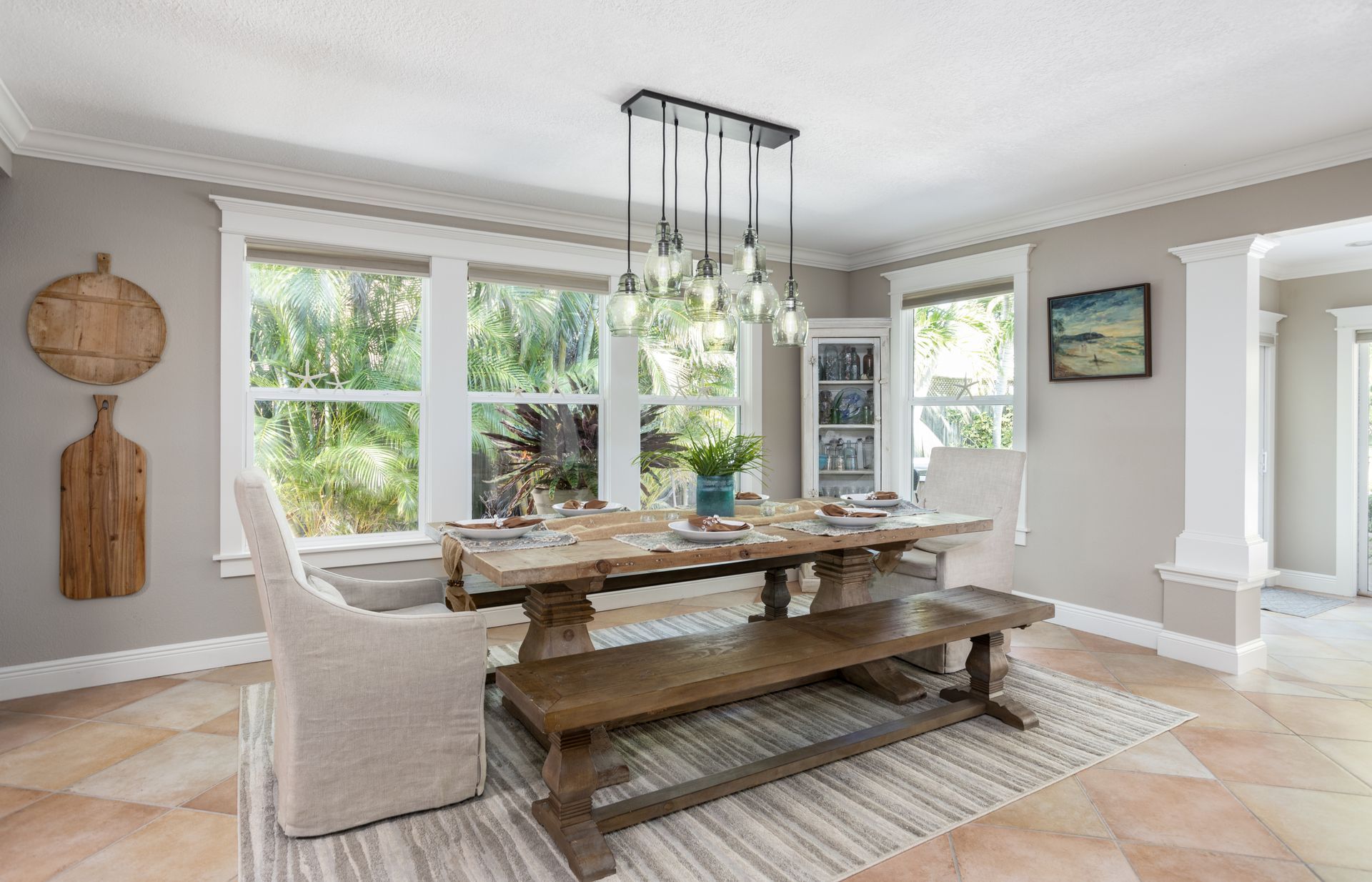 Bright dining room with rustic wooden table, beige chairs, and large windows overlooking greenery
