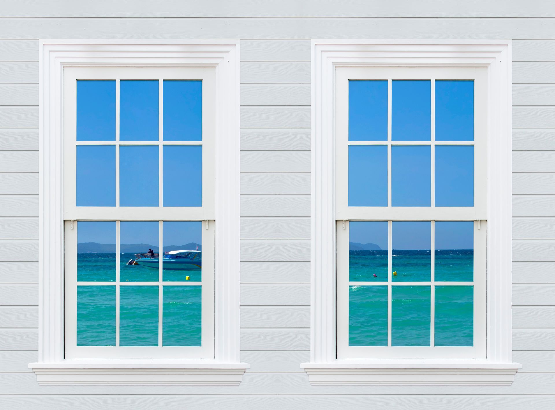 Two white windows with blue ocean views against a light gray siding wall