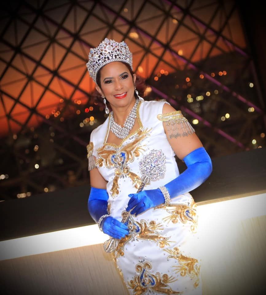 A woman in a white dress and blue gloves is wearing a crown