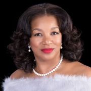 A woman wearing a white fur coat and a pearl necklace.