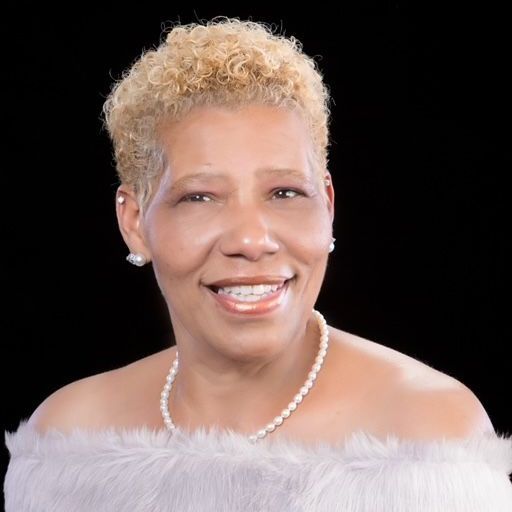 A woman wearing a fur coat and a pearl necklace is smiling.