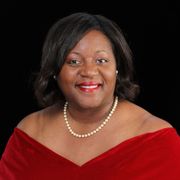 A woman wearing a red dress and a pearl necklace is smiling.