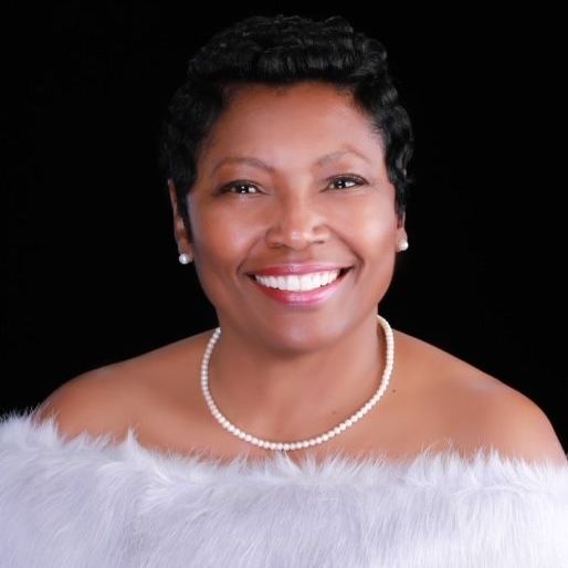 A woman wearing a white fur stole and a pearl necklace smiles for the camera