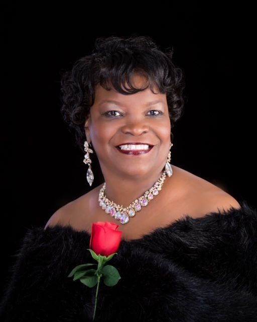 A woman in a black fur coat is holding a red rose