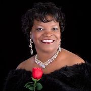 A woman wearing a necklace and earrings is holding a red rose.