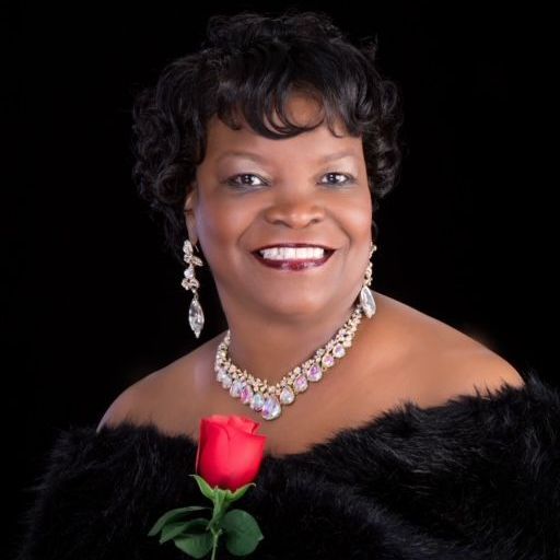 A woman wearing a necklace and earrings is holding a red rose.