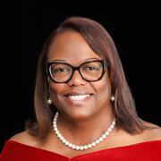 A woman wearing a red dress and a pearl necklace is smiling for the camera.