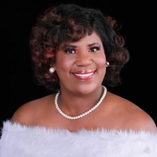 A woman wearing a pearl necklace and earrings smiles for the camera