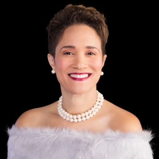 A woman wearing a fur coat and a pearl necklace is smiling.