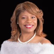A woman is wearing a white fur coat and a pearl necklace.