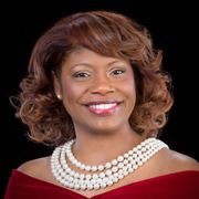 A woman wearing a red dress and a pearl necklace is smiling for the camera.