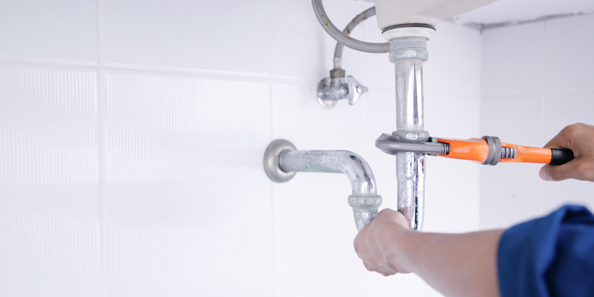 Plombier utilisant une clé sur des tuyaux sous un évier dans une salle de bain.