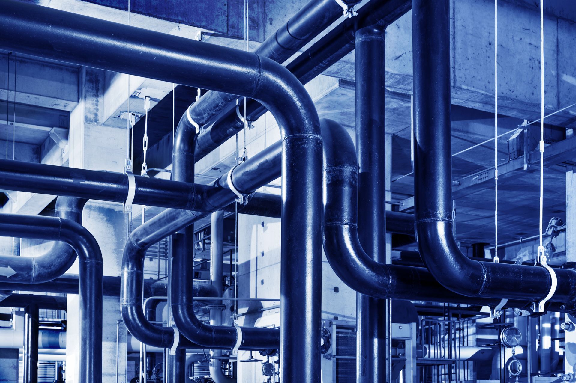 Dans un environnement industriel, des tuyaux industriels bleus, droits et courbes, courent le long d'un plafond.