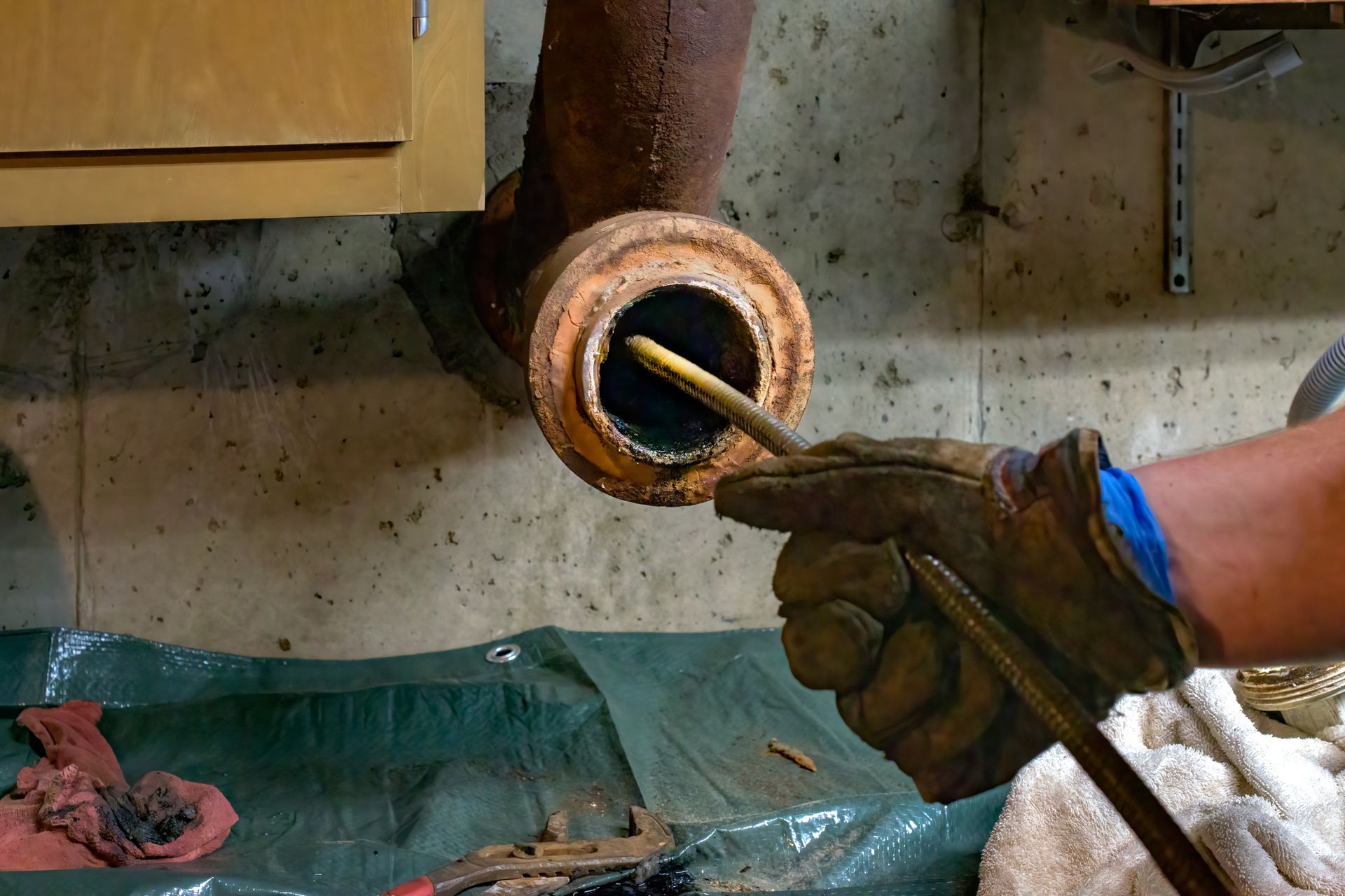 Une personne utilise une tige pour nettoyer un conduit de cheminée rouillé dans un sous-sol.