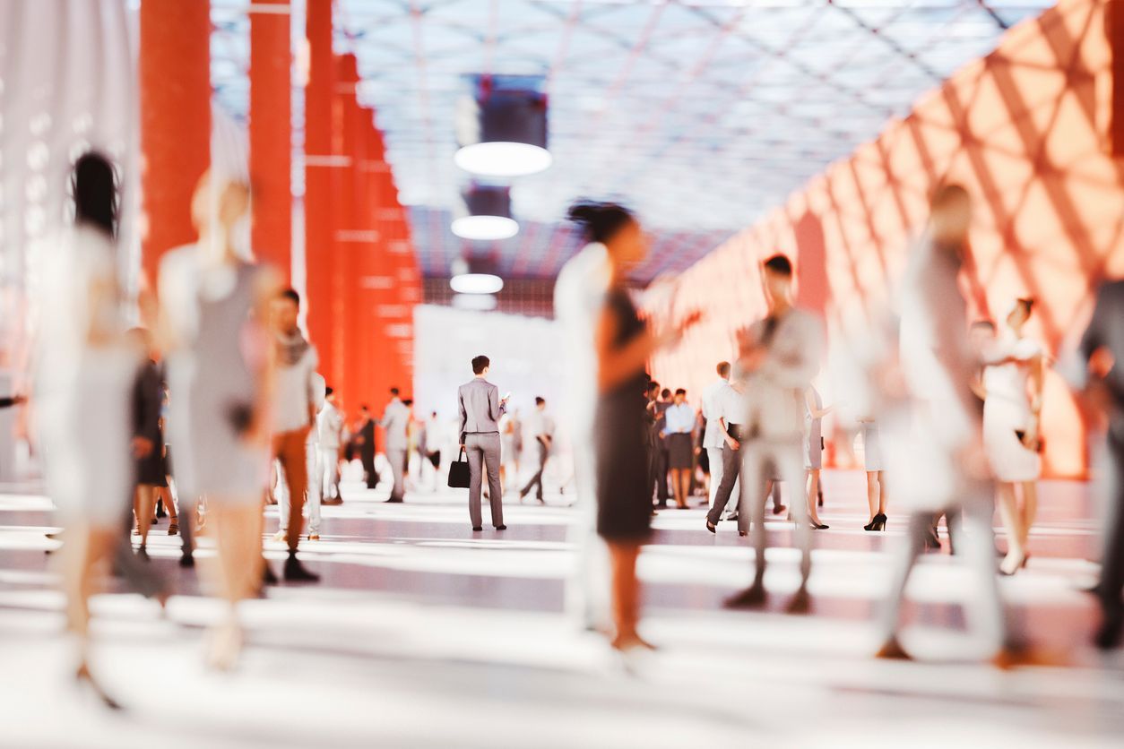 People walking in a bright, modern building with orange pillars; blurred effect.