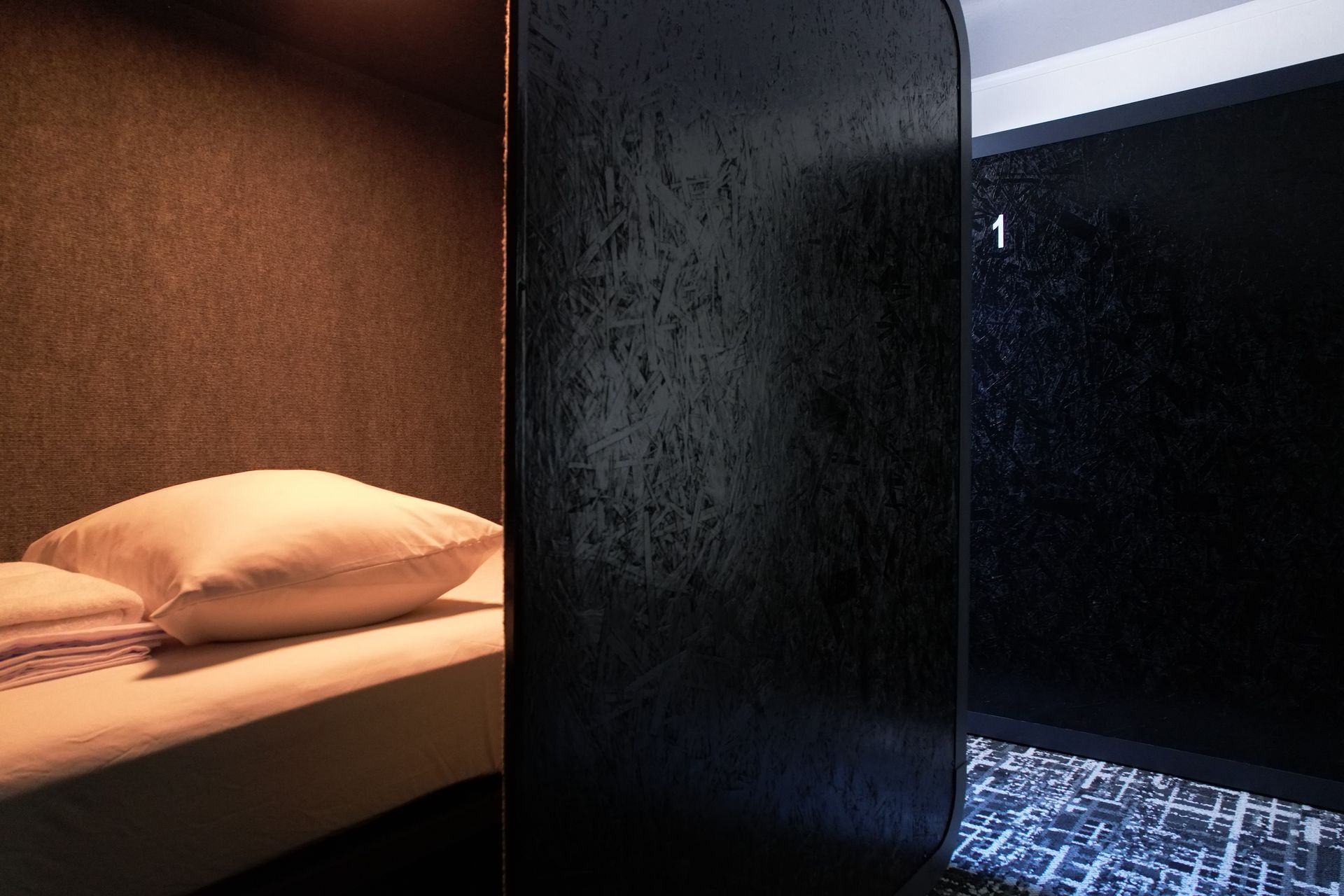 Hotel room with bed in a brown alcove, black partition, and dark door marked 