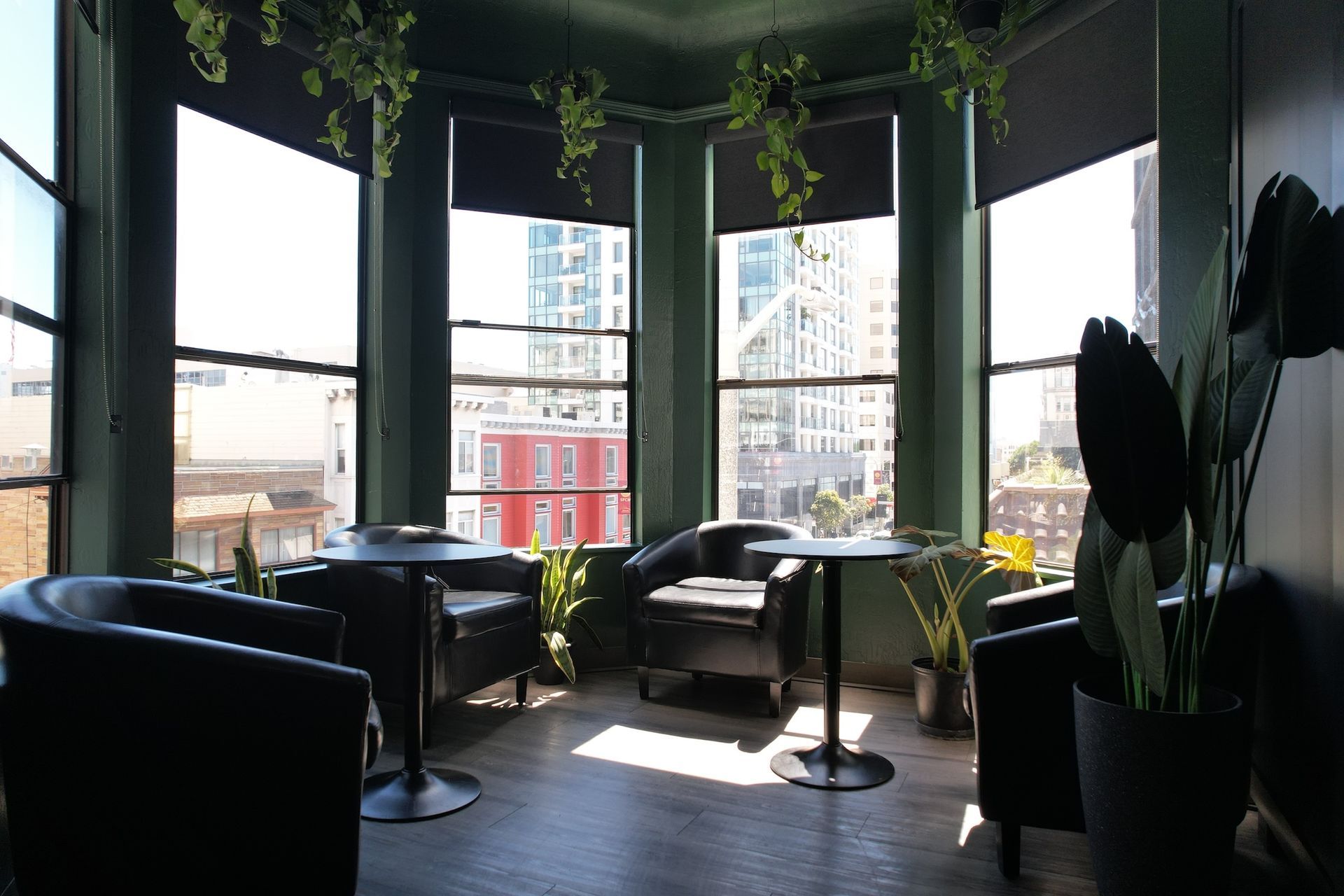 A lounge area with black chairs, small tables, and windows overlooking a city; greenery decorates the space.