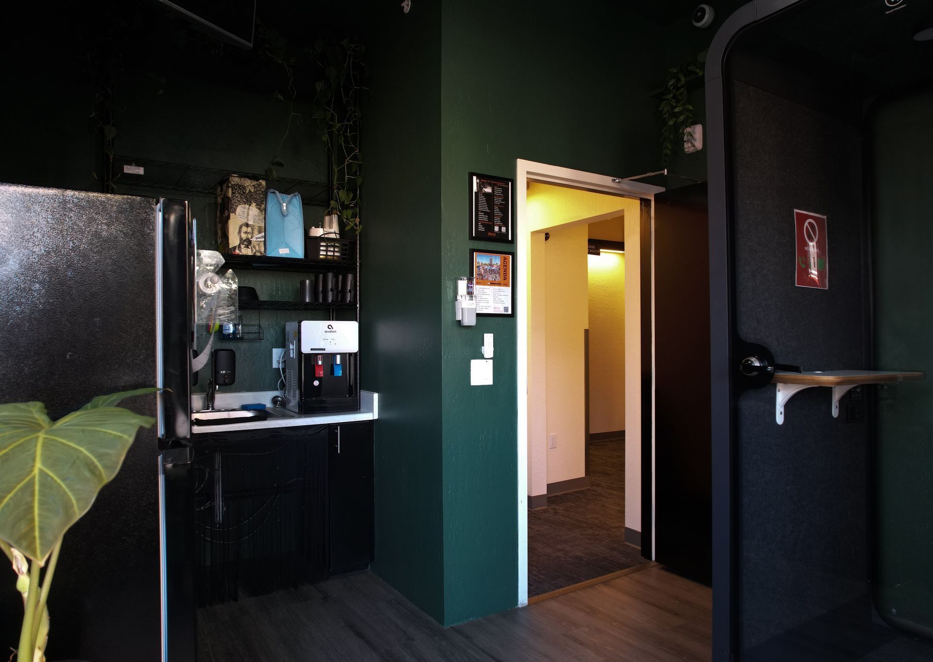 Dark green office interior with a kitchenette and open doorway.