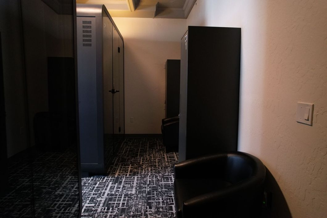 A narrow room with black cabinets, a black chair, and patterned flooring. A door is visible down the hallway.