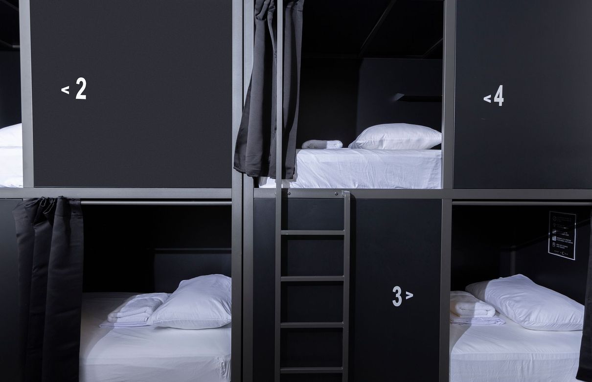 Dark-colored hostel beds stacked vertically with numbers beside each bed. Each bed has a white pillow and sheets.