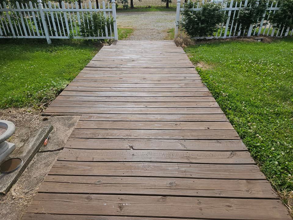 Wooden walkway leading through a grassy yard to a white picket fence and gate