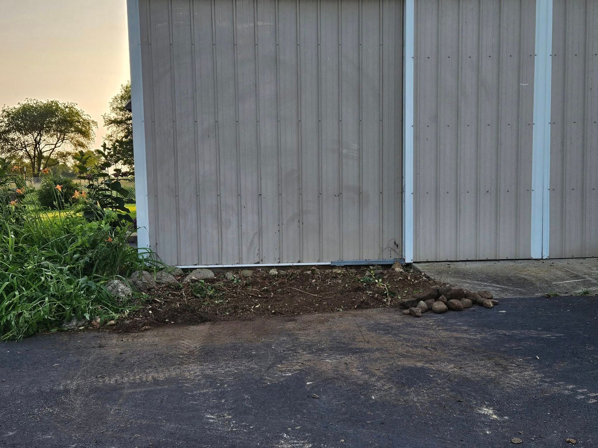 Weathered gray shed wall beside a gravel path with greenery and trees at left