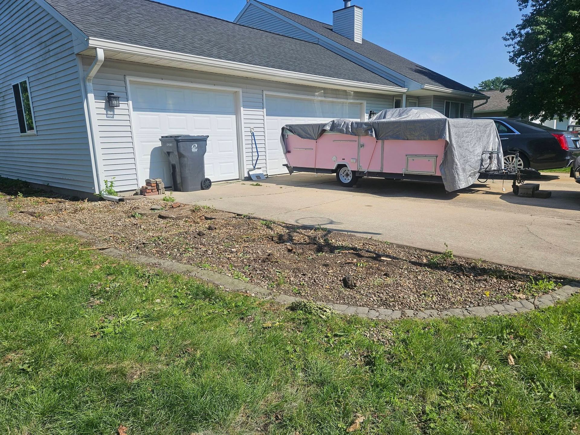 Pink trailer parked in a driveway beside a white garage and lawn under a blue sky
