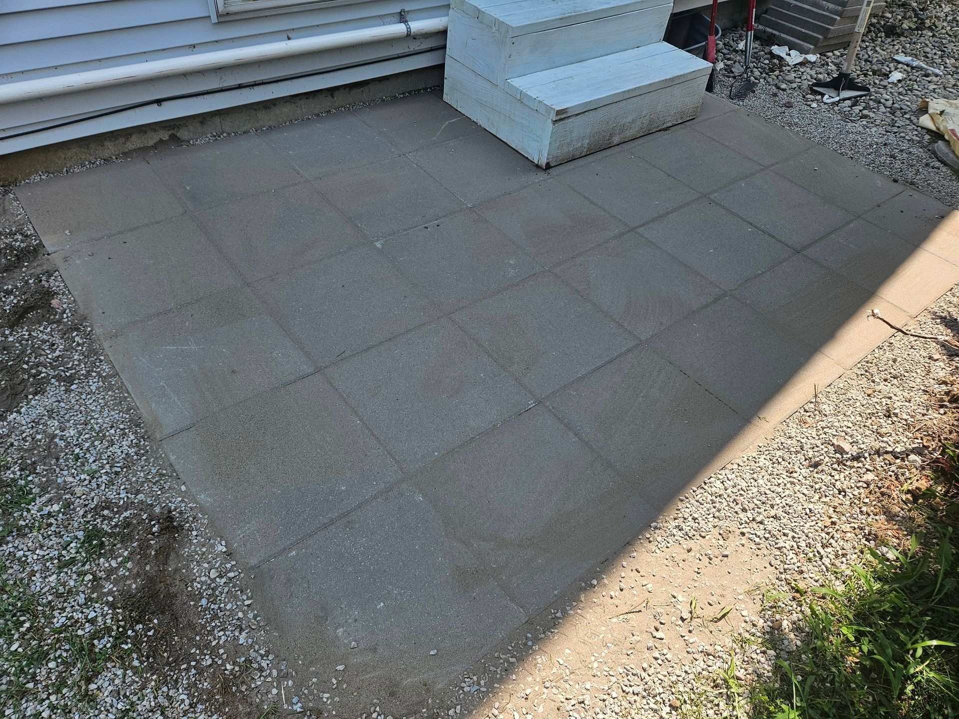 Small paved patio beside house steps, with a gravel border and some grass.