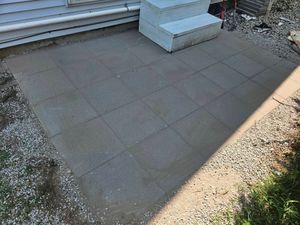 Small paved patio beside house steps, with a gravel border and some grass.