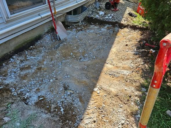 Freshly dug trench beside a house, with exposed soil and a red shovel handle.