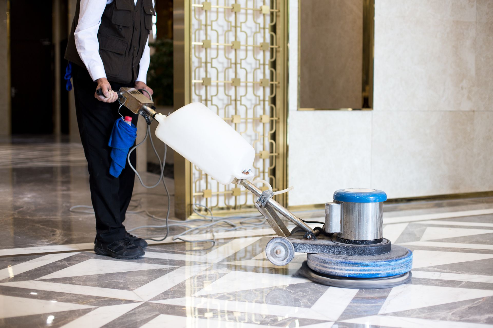Worker polishing a marble floor with a floor buffer in a bright hallway