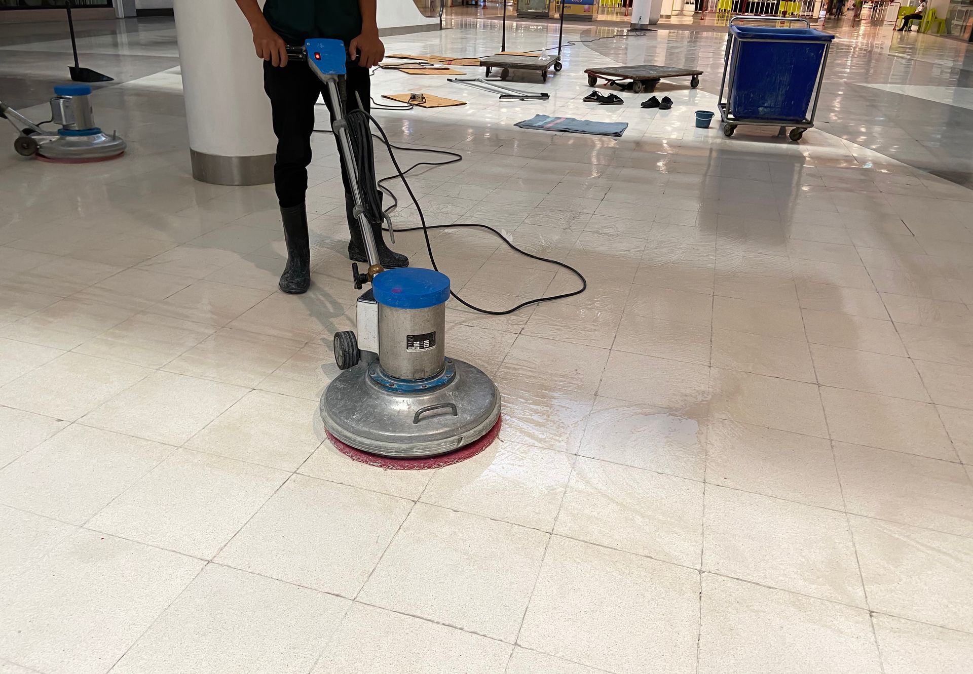 Worker using a floor buffer on a shiny mall floor with wet areas nearby