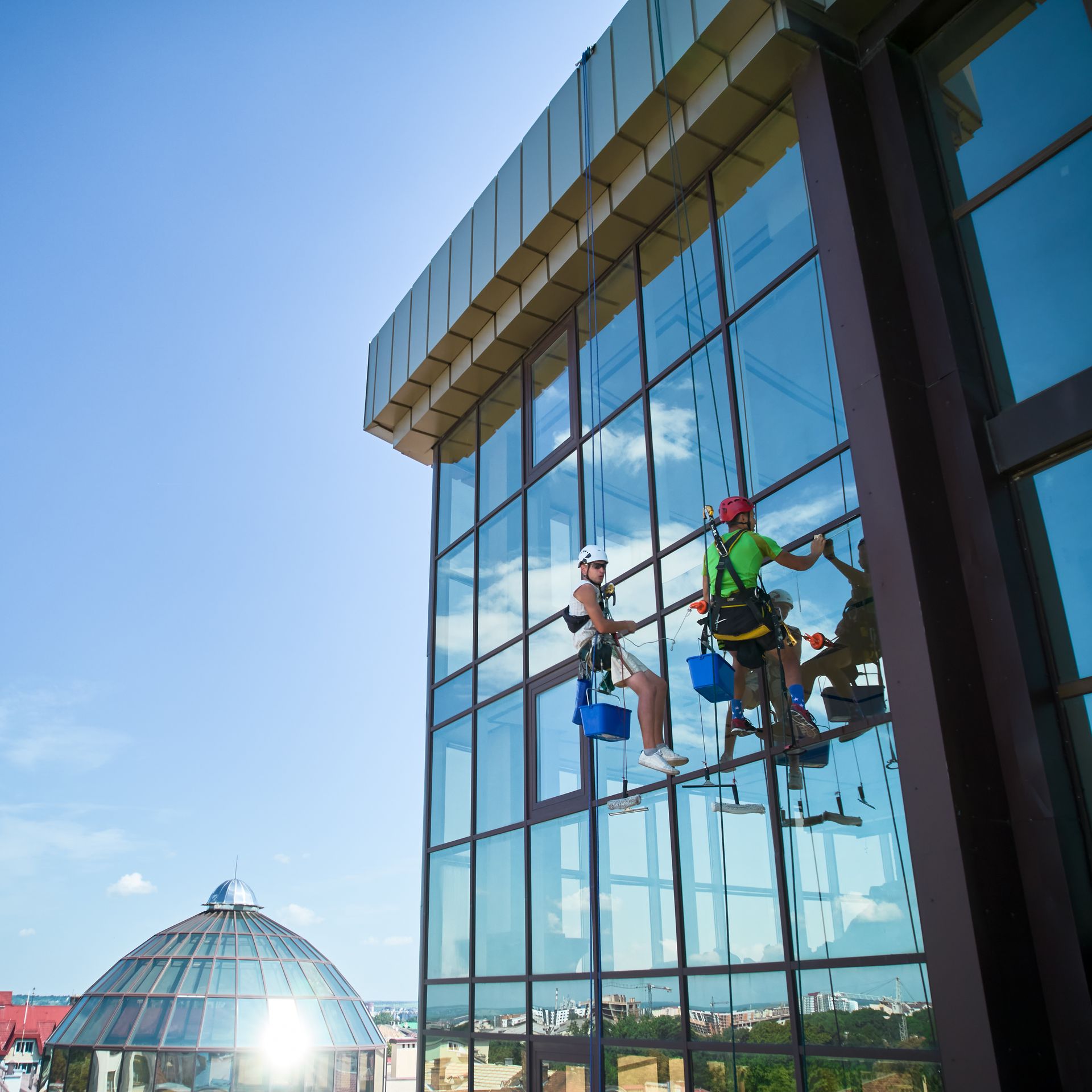 Two climbers on a glass office building under a blue sky